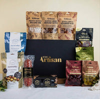 Assorted gourmet food items including nuts, olives, and truffles displayed in front of a Kiwi Artisan box.