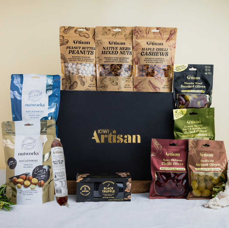 Assorted food products including nuts, olives, and truffles displayed in front of a Kiwi Artisan box.