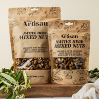 Two packages of Kiwi Artisan Native Herb Mixed Nuts on a wooden surface with greenery.