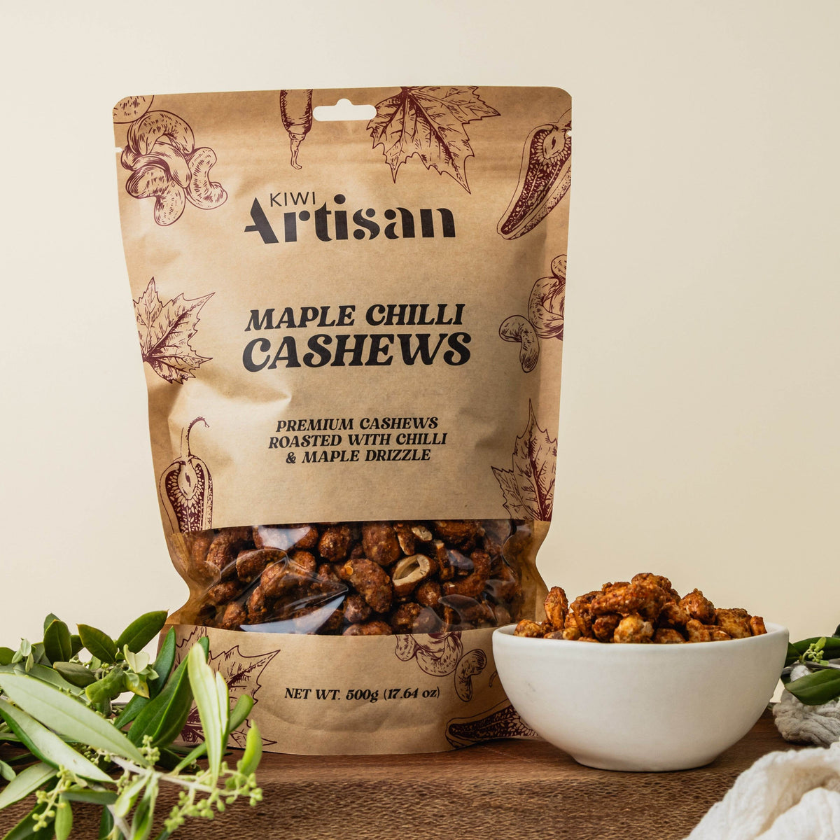 Bag of Kiwi Artisan Maple Chilli Cashews with a bowl of cashews on a wooden surface.