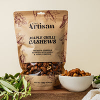 Bag of Kiwi Artisan Maple Chilli Cashews with a bowl of cashews on a wooden surface.