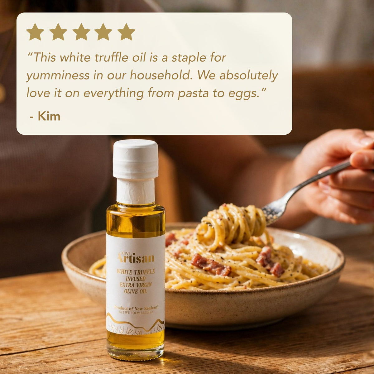 Bottle of white truffle oil next to a bowl of pasta with a quote from Kim on a wooden table.