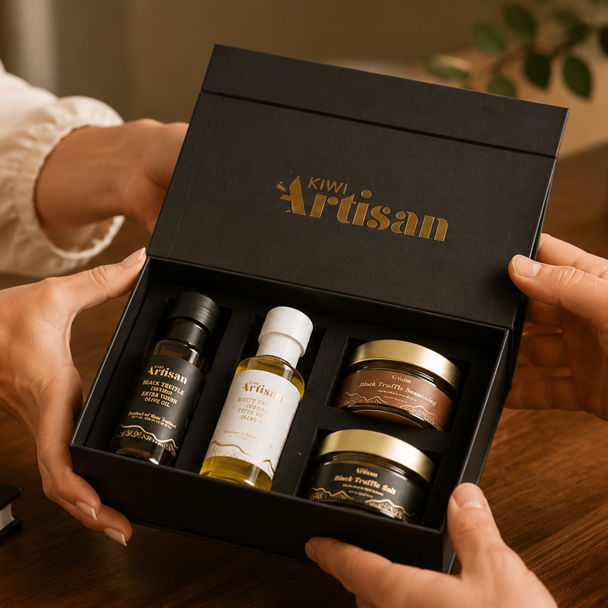 A black gift box labeled 'Tono Artisan' is held open by two people at a wooden desk, revealing several skincare or cosmetic bottles and jars inside. The scene is warmly lit and includes a laptop, notebook, and plant in the background.