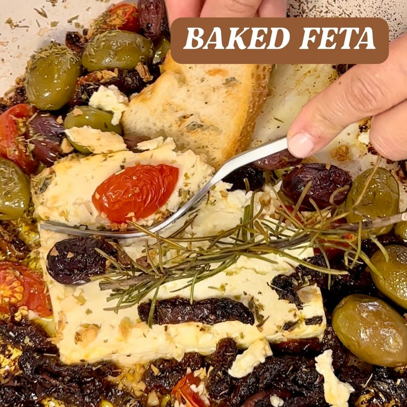Baked feta cheese with olives, tomatoes, and bread on a plate.