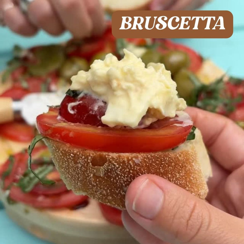 Bruschetta held in a hand with a blurred background of more bruschetta and ingredients.