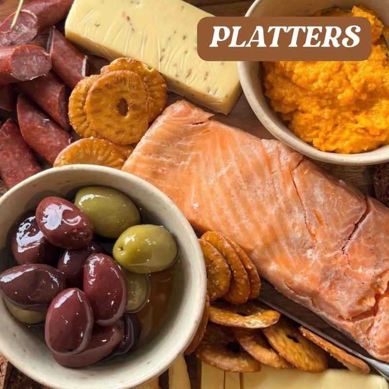 Assorted platter with salmon, olives, crackers, and cheese on a wooden board.
