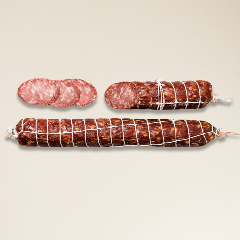 Two cured dry aged truffle salami, one sliced, on a beige background