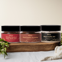 Three jars of Kiwi Artisan Truffle salt and truffle seasoning and manuka smoked flaky  chilli salt on a wooden board with a white background