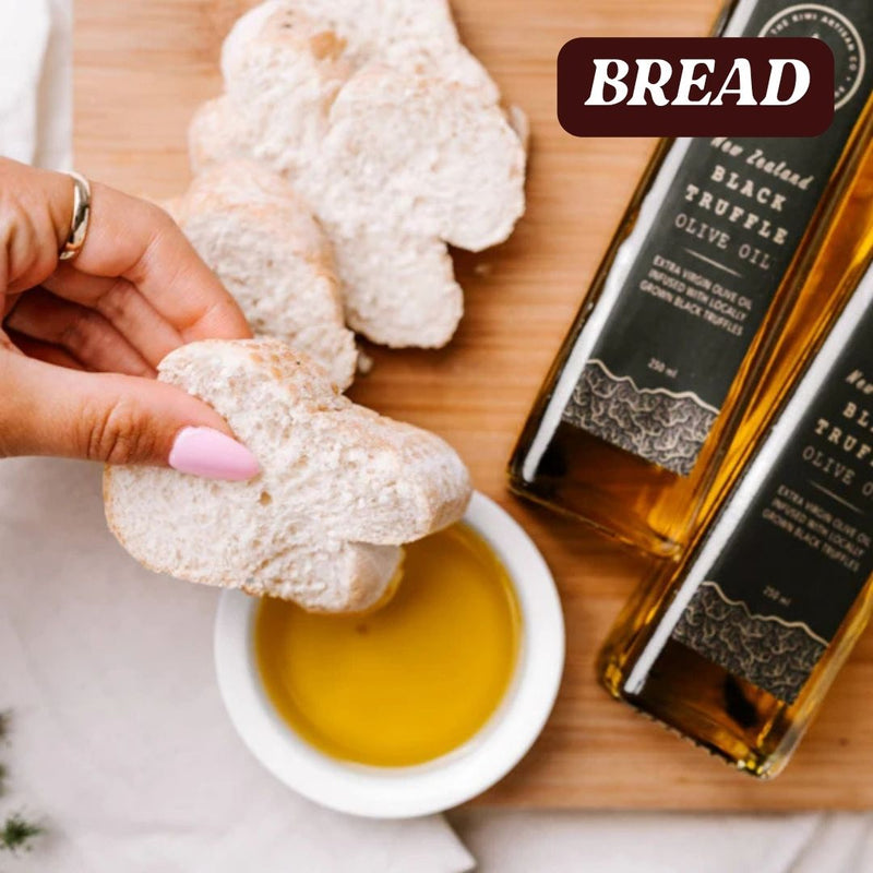 Bread being dipped into black truffle olive oil with a bottle of black truffle olive oil on a wooden board.