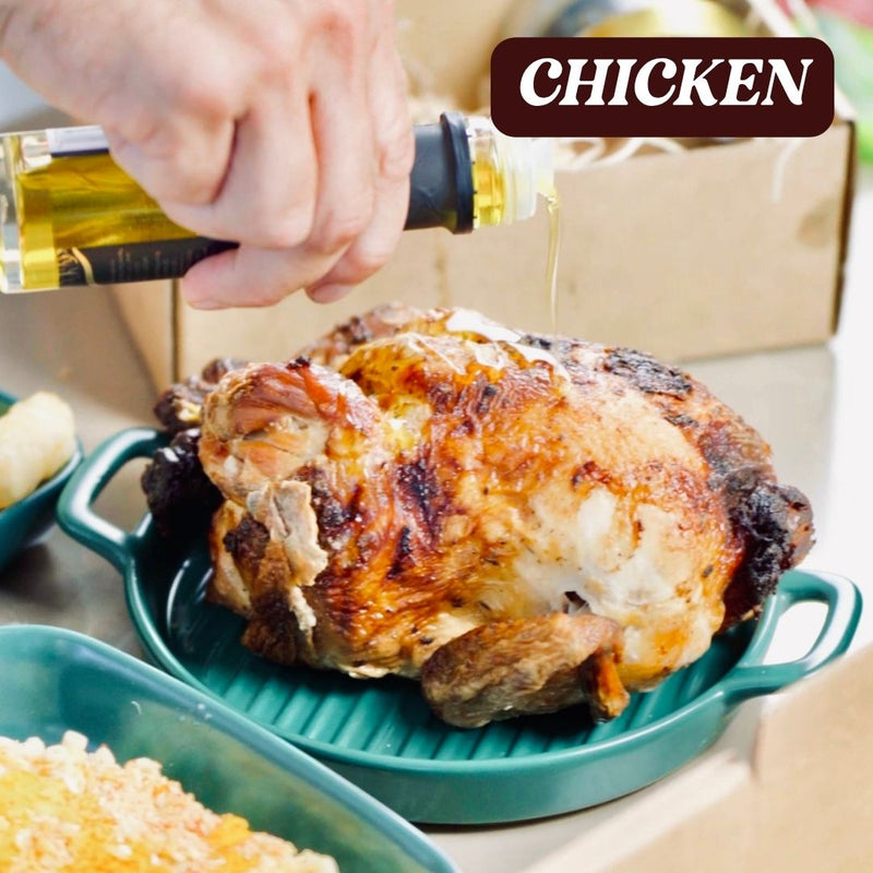 Roasted chicken being seasoned with a bottle of black truffle oil on a table.